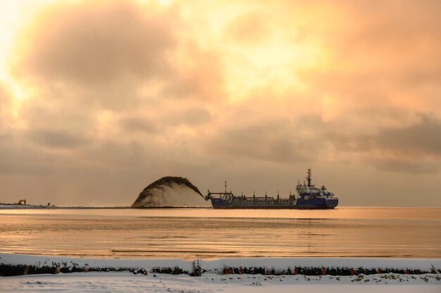 Schiff bei Baggerarbeiten. Bagger, der auf See arbeitet. Aushubmaterial aus einer Wasserumgebung versenden. Goldene Stunde. Bau Marine Offshore-Arbeiten. Dammbau, Kran, Lastkahn, Bagger.