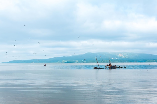 Schiffswrack vor dem Hintergrund einer Meeresbucht mit nebligen Bergen im Hintergrund