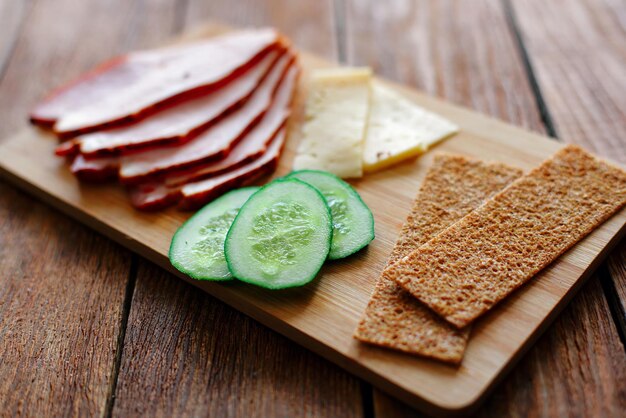 Foto schinken gurken und käse mit roten dünnen broten liegen auf einem holzbrett