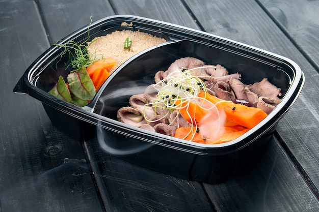 Schinken mit Couscous und Gemüse in Behältern auf schwarzem Holzhintergrund Diät zum Mitnehmen und gesunde Ernährung