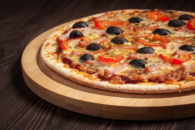 Schinkenpizza mit Paprika und Oliven auf Holzbrett auf dem Tisch aus nächster Nähe