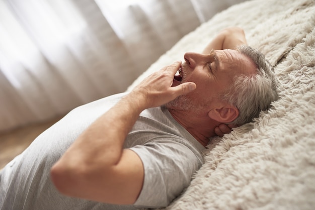 Schläfriger erschöpfter älterer Mann gähnt im Schlafzimmer.