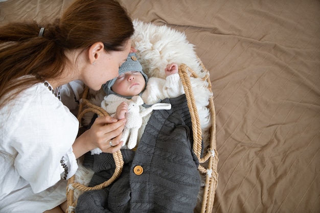 Schläfriges Baby in einer Weidenwiege in der Wärme nahe einer glücklichen fürsorglichen Mutter-Draufsicht.