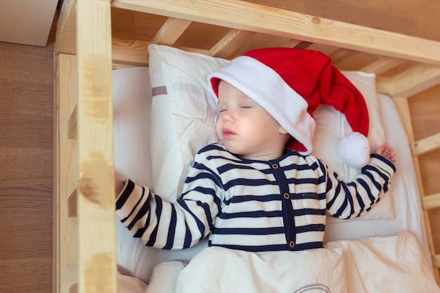 Schläfriges Baby in roter Weihnachtsmütze in seinem Bett