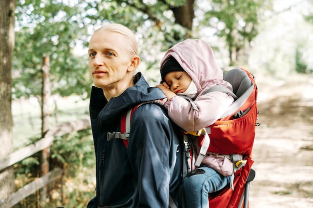 Schläfriges müdes Kind, das mit Vater im Rucksack draußen spaziert