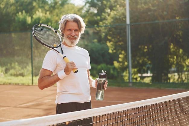 Schläger halten Älterer, moderner, stilvoller Mann mit Schläger im Freien auf dem Tennisplatz tagsüber