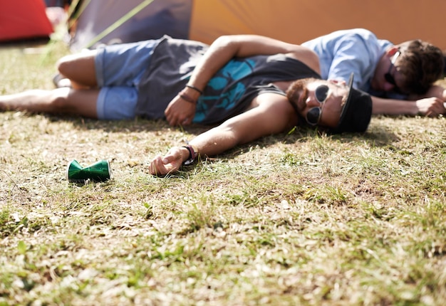 Schlafende Betrunkene und Männer auf dem Campingplatz bei einem Musikfestival mit Alkohol. Trinken auf dem Feld und auf dem Rasen mit einem Zelt und Jugendliche auf dem Rasen mit Menschen und ein Mann, der mit Dosen auf einem Konzert im Freien campt