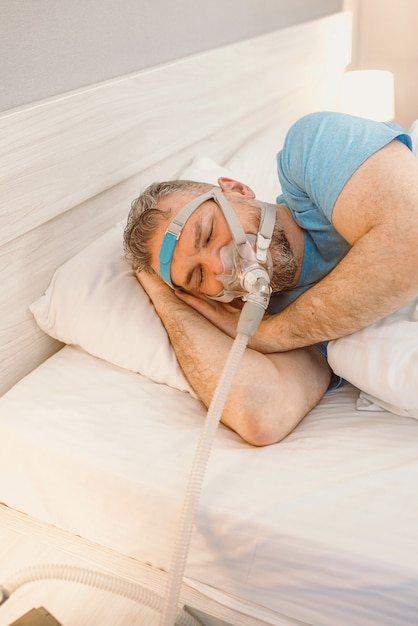 Schlafender Mann mit chronischen Atemproblemen mit CPAP-Gerät im Bett