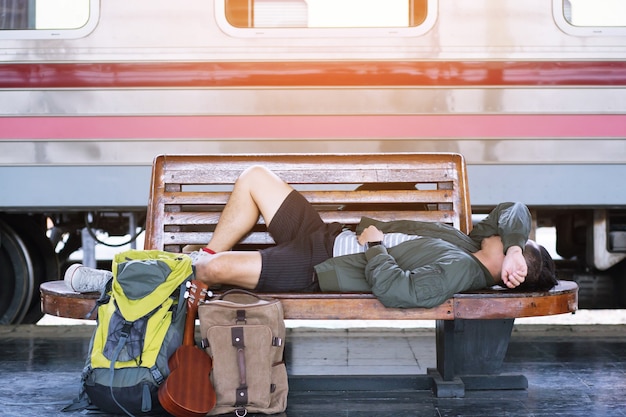 Schlafender schlaf des jungen mannreisenden auf stuhl im wartenden zug des bahnhofs gehen, um zu reisen, urlaub