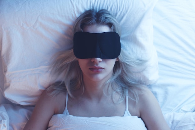 Schlafendes Mädchen in einer Schlafmaske auf einem orthopädischen Kissen unter Nachtbeleuchtung, weiße Bettwäsche, Draufsicht