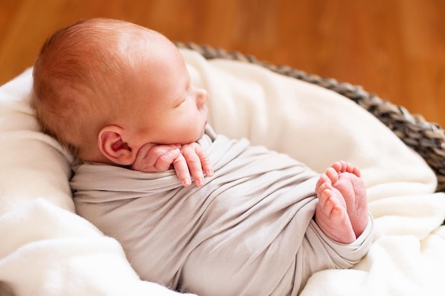 Schlafendes neugeborenes Baby im grauen Korb. Kleine Hände und Füße des Kindes. Babyverpackung.