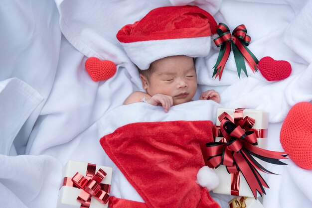 Schlafendes neugeborenes Babygesicht im Weihnachtshut mit Geschenkbox von Santa Claus