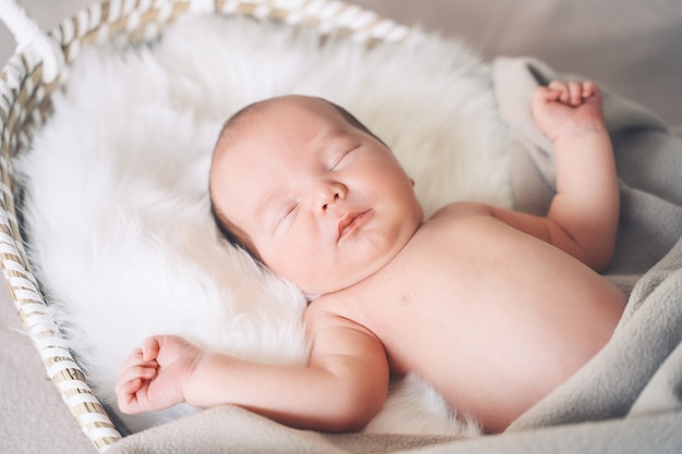 schlafendes Neugeborenes im Korb in Decke im weißen Pelzhintergrund gewickelt