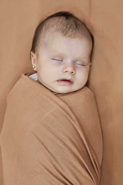 Schlafendes neugeborenes Mädchen, eingewickelt in eine braune Decke