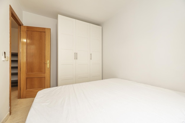 Schlafzimmer mit einem Doppelbett und einem weißen dreiteiligen Kleiderschrank und einer Eichentür