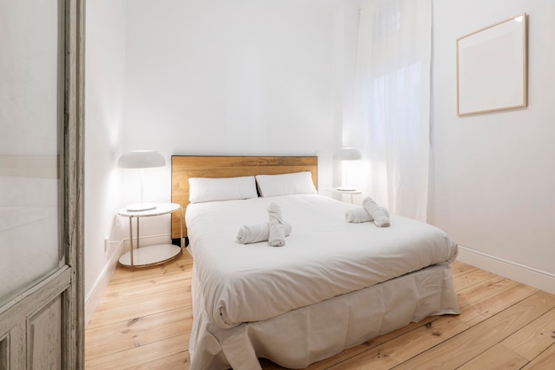 Schlafzimmer mit Kingsize-Bett mit weißer Bettwäsche und hölzernem Kopfteil mit schwarzen Akzenten, weißen Lampen und weißen Leinenvorhängen mit schönem Kiefernholzboden und Holztür