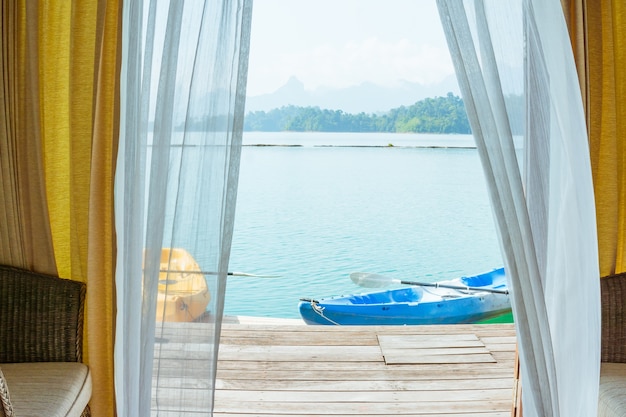 Schlafzimmeransicht mit Fenstervorhang und Kajak auf einem See und einem Berg.