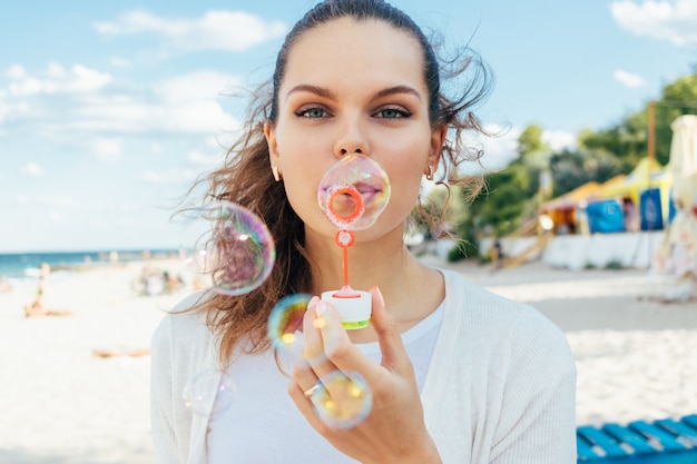 Schlagblasen der jungen Frau auf dem Strand im Sommer