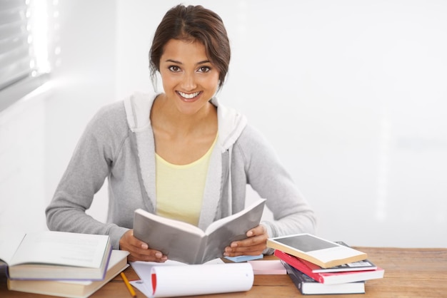 Schlagen die Bücher mit einem Lächeln auf ihrem Gesicht Porträt einer hübschen jungen Universitätsstudentin, die für ihre Prüfungen in ihrem Schlafsaal studiert