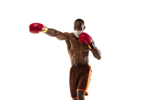 Schlagen Sie das Virus ab. Afroamerikanischer Boxer in Schutzmaske, Handschuhen. Auch während der Quarantäne aktiv. Gesundheitswesen, Medizin, Sportkonzept.