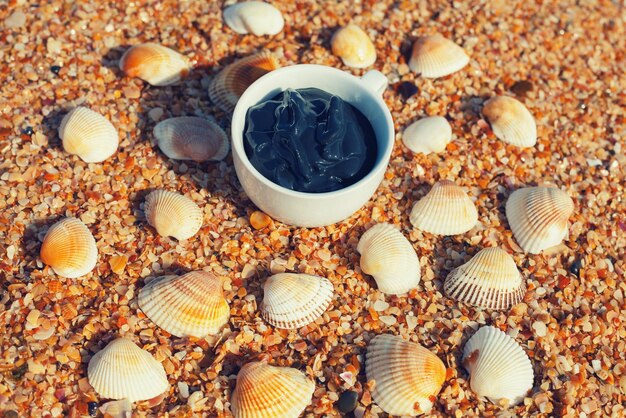 Schlamm aus dem Toten Meer für Spa-Behandlungen in einer Tasse am Strand mit Muschel