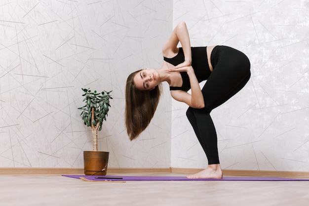 Schlanke Frau, die barfuß auf Matte in Revolved Chair-Pose steht