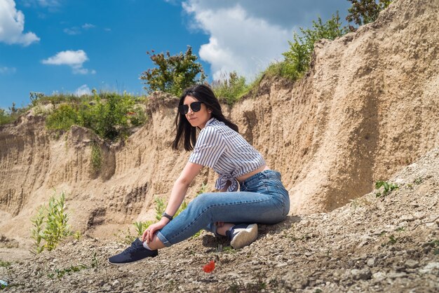 Schlanke junge Frau, die auf Sand nahe dem Felsen im Steinbruch oder in der Schlucht steht. Sommerzeit für Ihre perfekte Reise