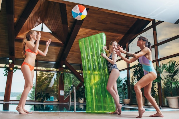 Schlanke junge Frauen, die mit einem Strandball am Innenpool spielen