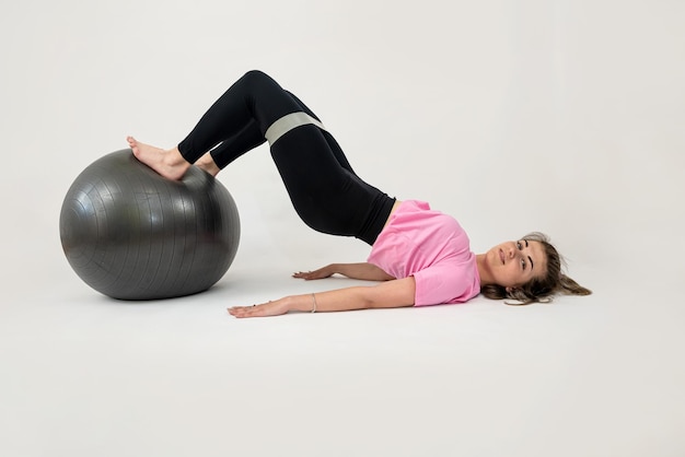 Schlanke kaukasische Frau macht Übungen mit Gummibändern und Fitnessball, der auf Weiß isoliert ist