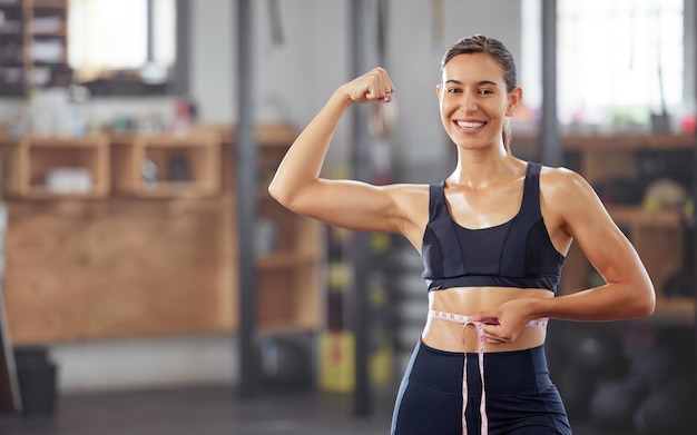 Schlanke Passform und Gewichtsverlust mit einer Frau, die ein Maßband um die Taille hält und ihre Muskeln beugt, um das Abnehmen zu feiern und ihr Ziel zu erreichen Lächelnde Sportlerin, die sich über Ernährung und Bewegung freut