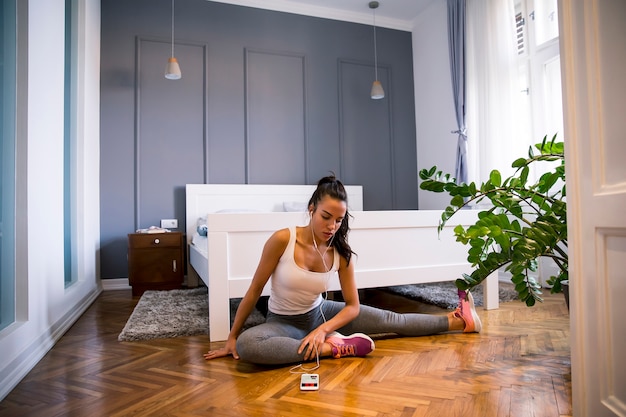 Schlanke Sportlerin in Sportbekleidung, die vor dem Training Dehnübungen macht, während sie zu Hause auf dem Boden sitzt