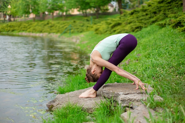 Schlanker junger Brunettejogi führt komplexe Yogaübung auf grünem Gras durch