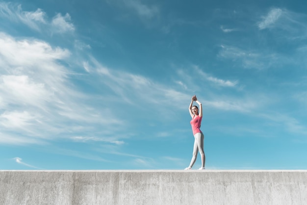 Schlankes, athletisches Mädchen, das sich unter dem blauen Himmel aufwärmt, führt einen aktiven und gesunden Lebensstil