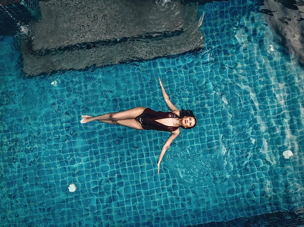 Schlankes Mädchen im sexy Badeanzug, das sich auf der Oberfläche des klaren Wassers im Pool entspannt; Modekonzept.