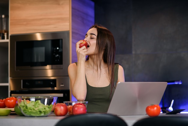 Schlankes nettes Brunette-Mädchen, das einen Apfel isst