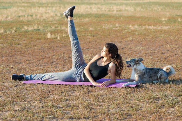 Schlankes sportliches Mädchen führt Dehnübungen in der Natur durch, die auf einer lila Yogamatte sitzt