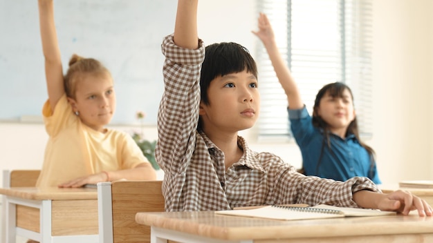 Schlauer Junge hebt die Hand, um Fragen zu stellen und zu beantworten Lehrer im Klassenzimmer Pädagogik