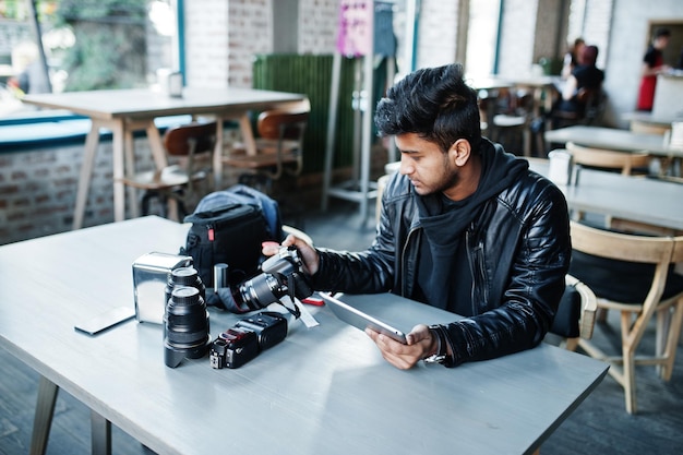 Schlauer junger asiatischer Mannfotograf, der mit Tablette beim Sitzen am Café arbeitet