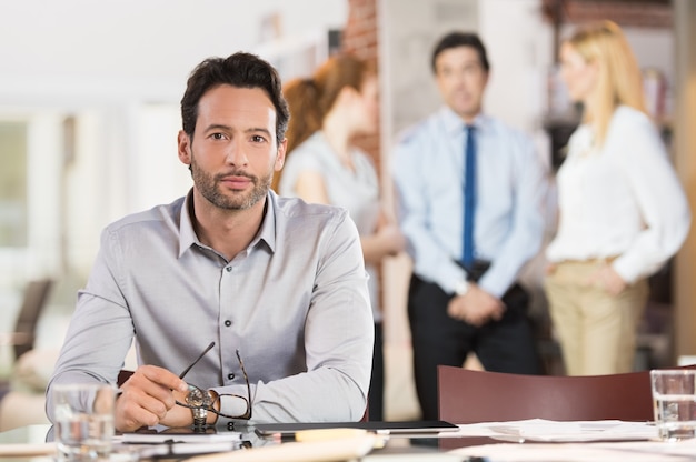 Schlauer junger Geschäftsmann, der Kamera in einer Besprechung im Büro betrachtet.