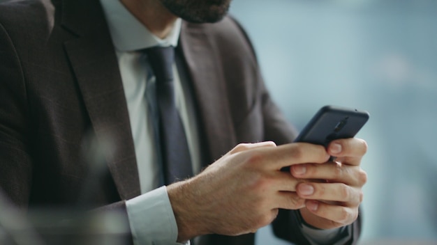 Schlauer Unternehmer textet mit dem Handy, sitzt im Büro und macht eine Nahaufnahme von einem Manager, der das Telefon benutzt.