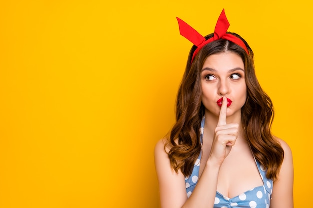 Schlaues hübsches Mädchen legte Finger auf Mundshow-Schweigensymbol auf gelbem Hintergrund