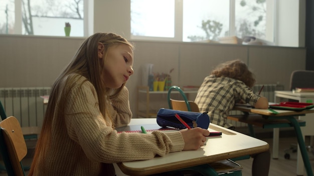 Foto schlaues schulmädchen schreibt in einem notizbuch im unterricht in der grundschule