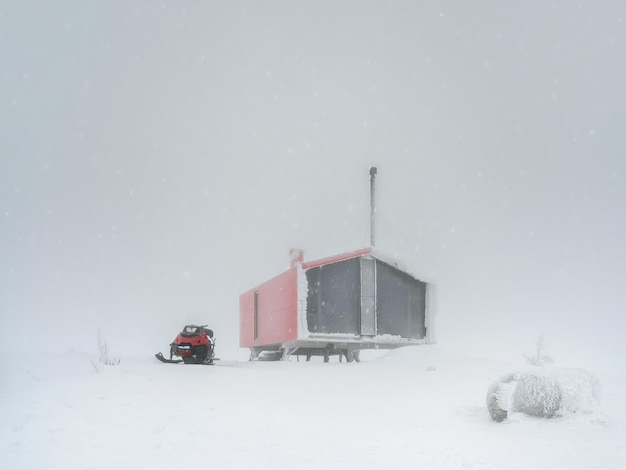 Schlechte Sicht bei Schneefall Gefrorenes Haus Rotes Haus und ein Schneemobil auf einem nebligen schneebedeckten Berg Winterurlaub extreme Abenteuer im Winter