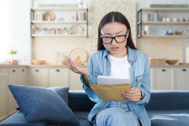 Schlechter Brief von der Bankfrau, die zu Hause sitzt, enttäuscht und traurige Lesenachricht schlechte Nachrichten asiatische Frau