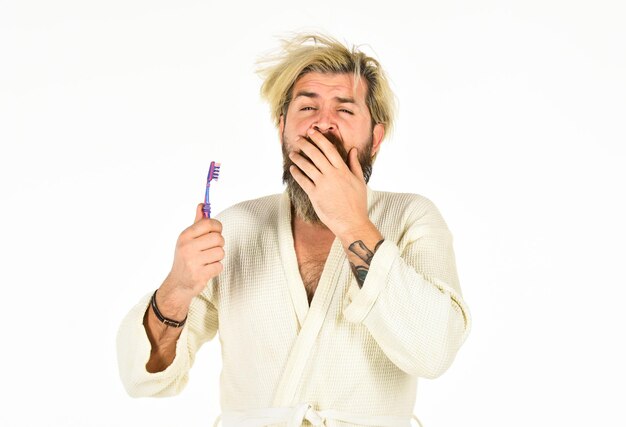 Schlechter Geruch Morgenroutine Mundhygiene Mann im Bademantel hält Zahnbürste Körperpflege Bärtiger Hipster beim Zähneputzen Frische und Sauberkeit Halten Sie die Zähne gesund Gesunde Gewohnheiten Zähne putzen