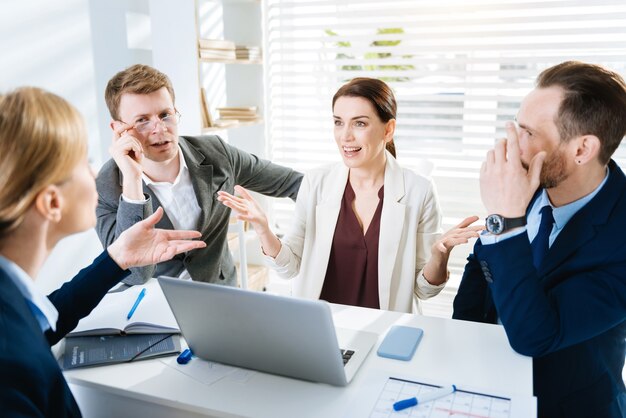 Foto schlechter partner. homosexuell attraktive vier kollegen sprechen, während sie gestikulieren, während sie am tisch sitzen