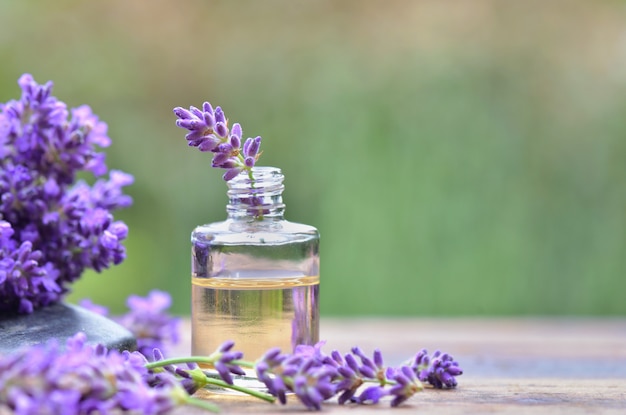 Schließen Sie auf lila Lavendelblume in einer Flasche des ätherischen Öls auf einem Tisch im Garten
