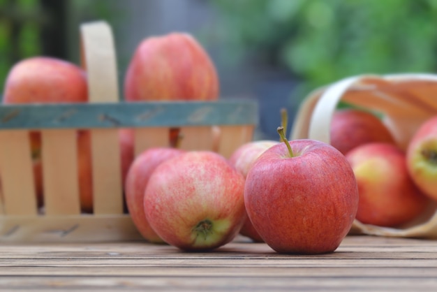 Schließen Sie auf roten Äpfeln im kleinen Korb auf einem Holztisch im Garten auf grünem Hintergrund