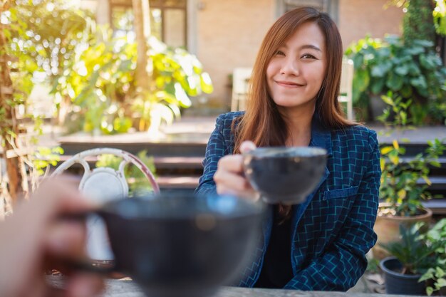 Schließen Sie das Bild einer schönen asiatischen Frau, die mit einem Freund im Café Kaffeetassen anstößt