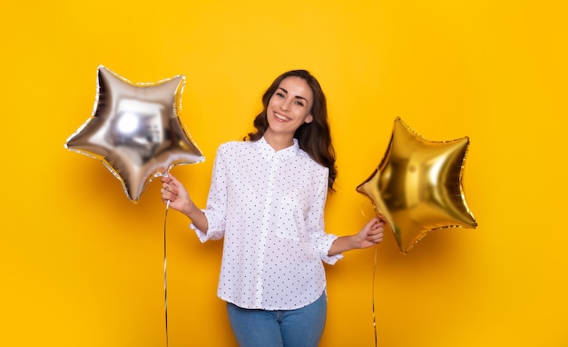 Schließen Sie das Porträt einer schönen glücklichen Frau, während sie mit zwei Ballons in Form von Sternen in ihren Händen posiert und etwas feiert